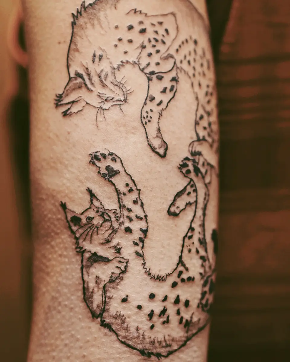 Tattoo of two playful spotted cats facing each other on a person's skin.