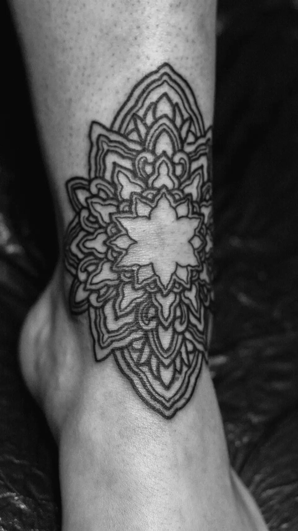 Black ink mandala tattoo with intricate geometric patterns on the ankle.
