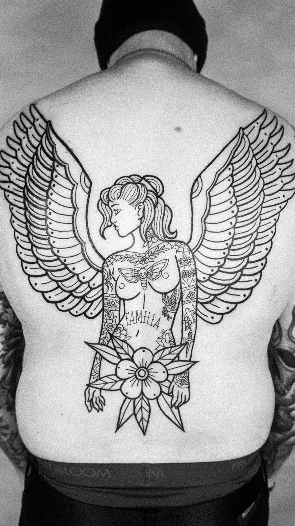 Large black ink tattoo of a winged woman with detailed floral and symbolic designs covering a person's full back.