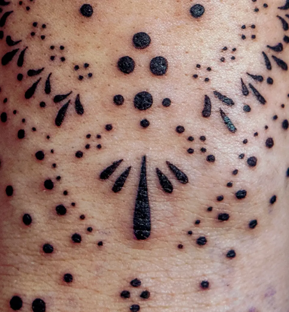 Close-up of a hand tattoo featuring black dot and teardrop shapes arranged in a symmetrical pattern on skin.