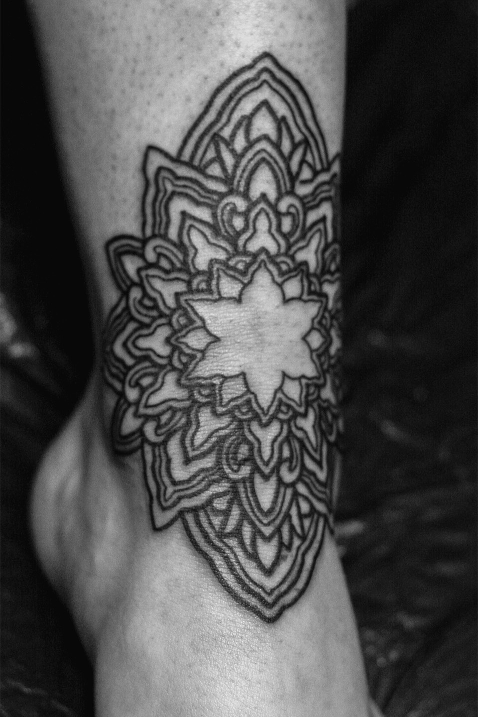 Tattoo of a stylized tree with intricate roots and branches, featuring a circular swirling center and surrounded by abstract geometric designs and binary numbers.