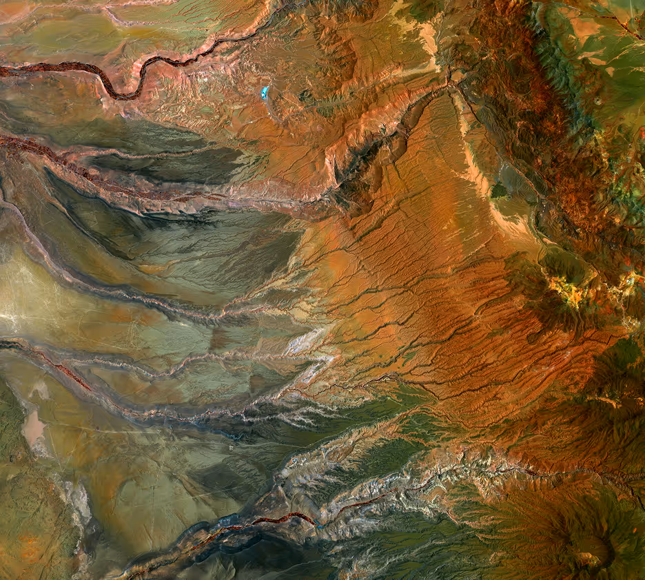 Satellite view of a rugged desert landscape with deep canyons and varied reddish and greenish terrain.