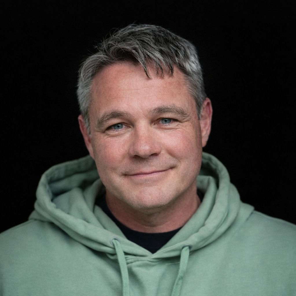 Smiling middle-aged man with gray hair wearing a light green hoodie against a black background.