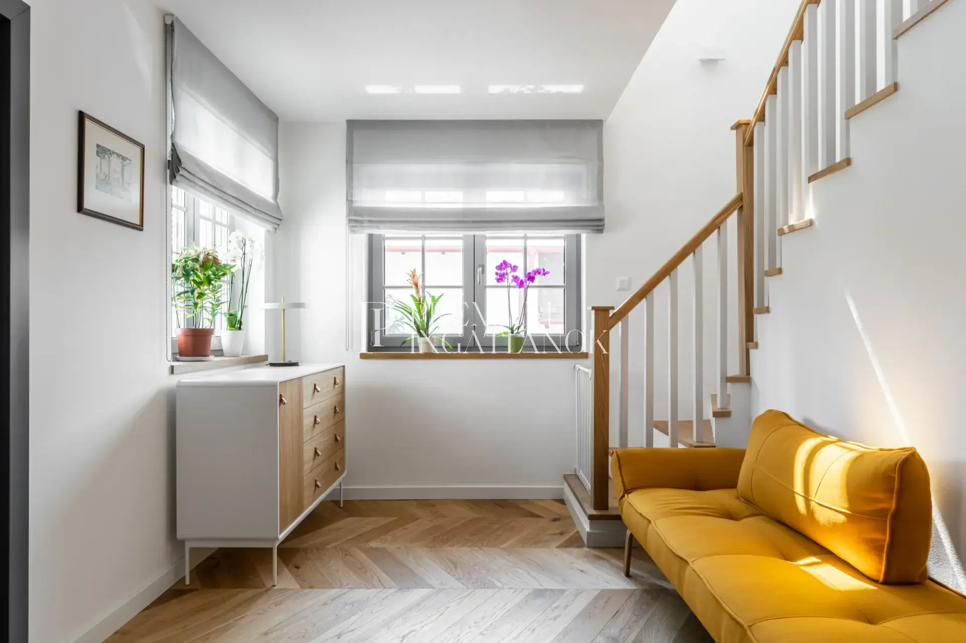 Minimalista belső tér napsárga modern kanapéval, absztrakt festménnyel és elegáns tölgyfa lépcsővel a szári házban