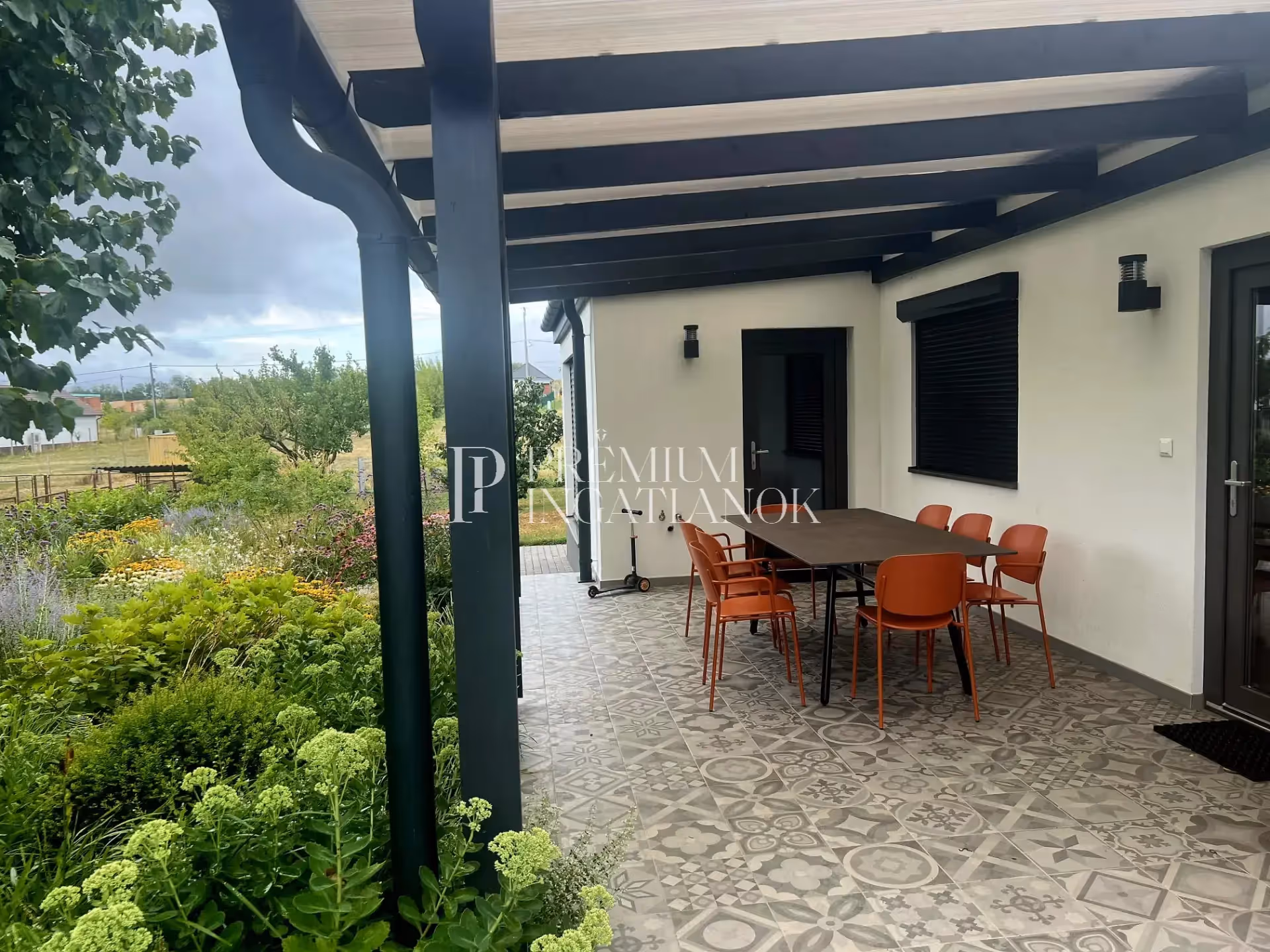 Modern, fedett terasz narancssárga design székekkel és kilátással a szári ingatlan buja kertjére.