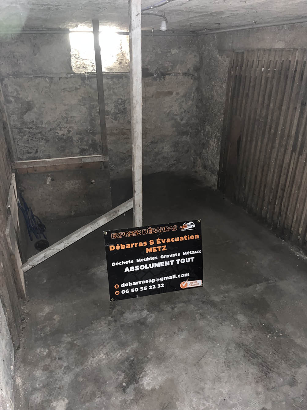 Empty basement room with concrete floor and stone walls featuring a sign for Express Débarras clearance and evacuation services.