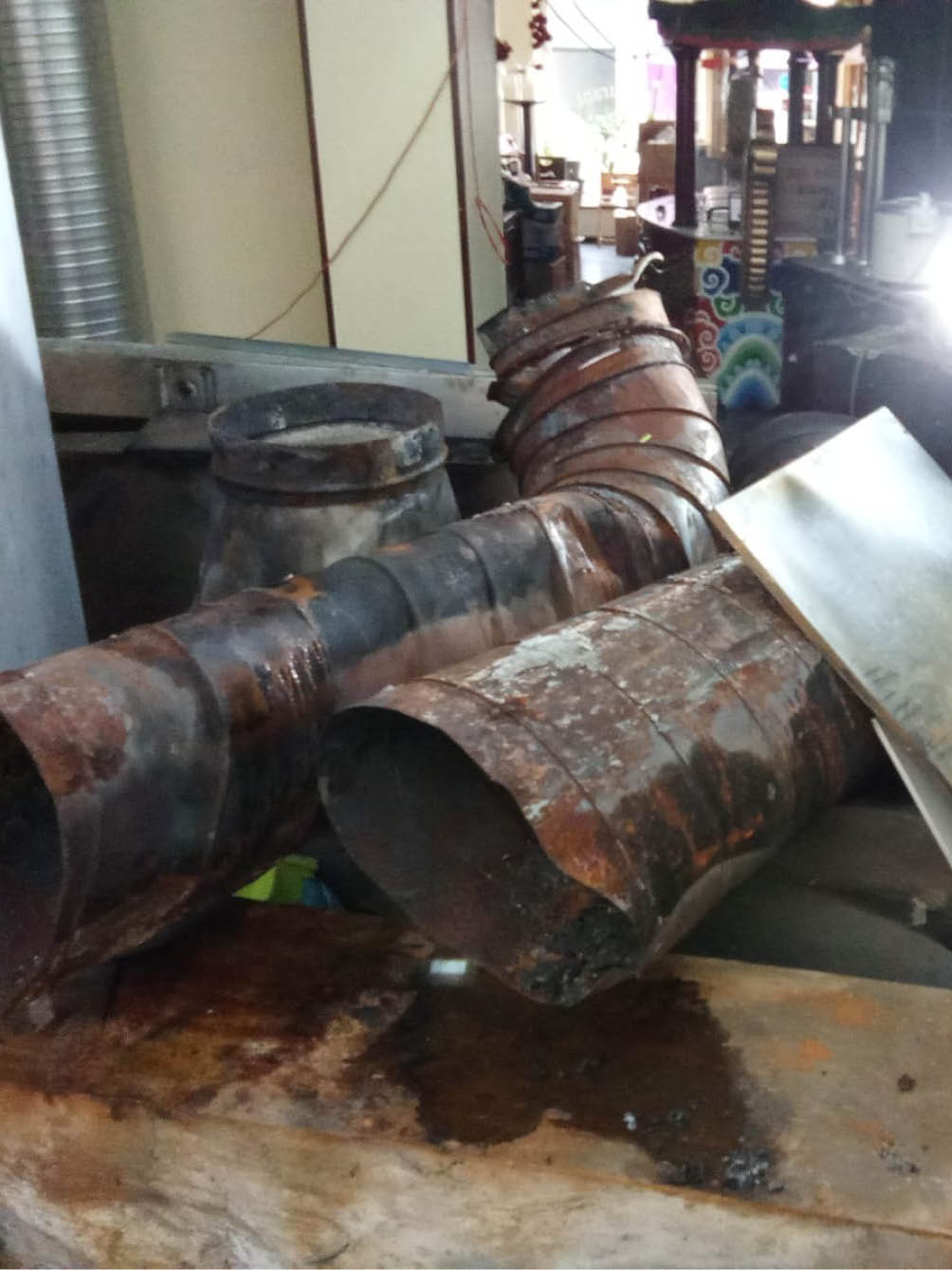 Rusty and bent metal ventilation ducts resting on a wooden surface in an industrial or workshop setting.