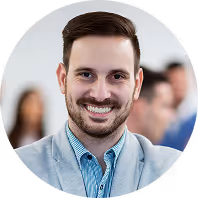 Lächelnder Mann in grauem Sakko, unscharfer Hintergrund mit weiteren Personen im Gespräch.