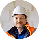 Bauarbeiter mit Helm und orangener Sicherheitsjacke lächelt in einer Baustellenumgebung.