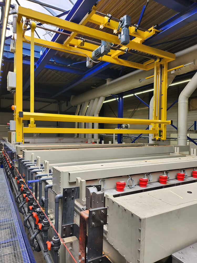 Gele industriële kraan boven elektrisch apparaat met buizen en kleppen in een fabriekshal.