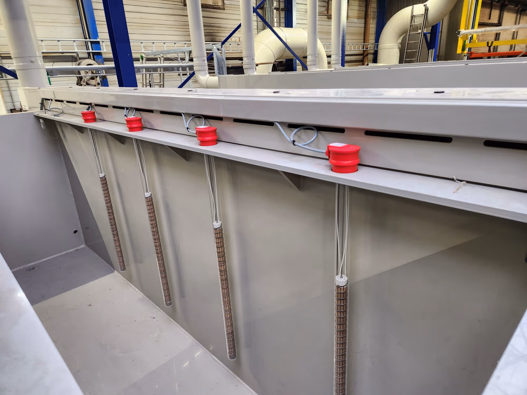 Vijf verticale bedradingstangen hangen aan een grijze metalen structuur in een industriële ruimte.