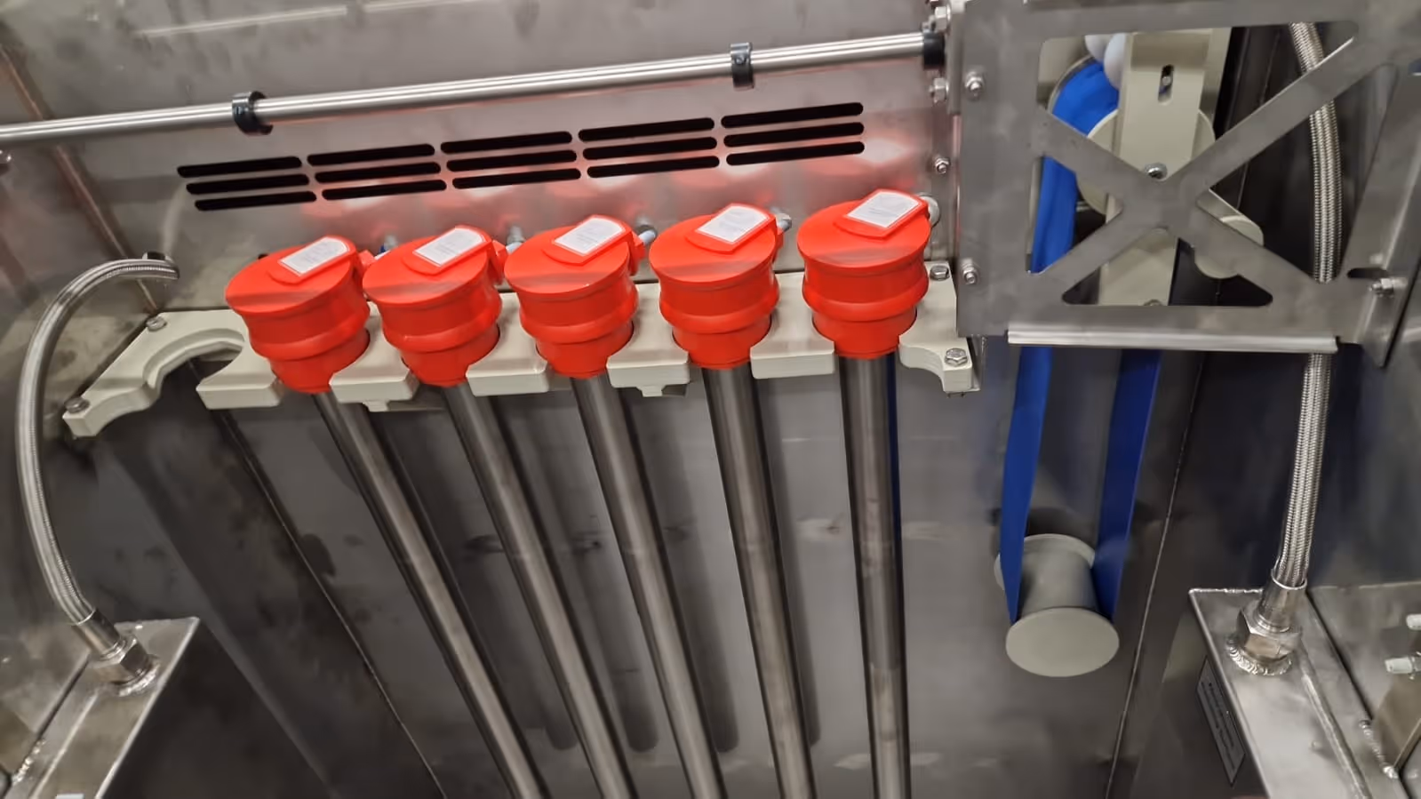 Vijf langwerpige metalen buizen met rode doppen gemonteerd in een industriële machine.