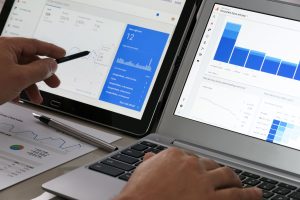 A person writing notes beside a laptop displaying an analytics dashboard