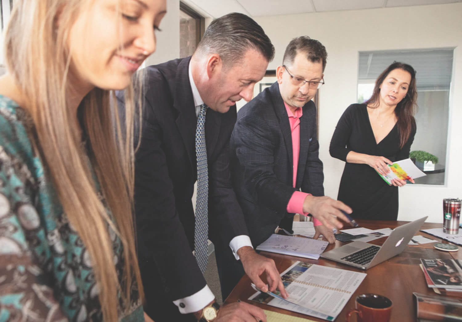 A group gathered around a laptop reviewing materials together in an office