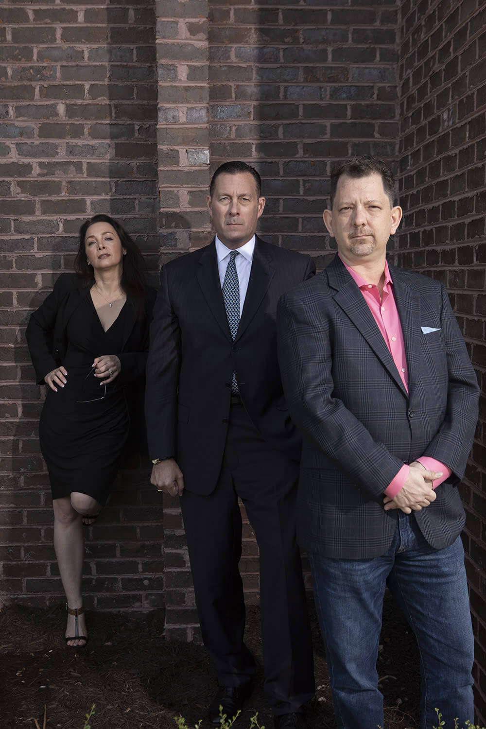 Four people in dark clothing photographed in front of a brick wall