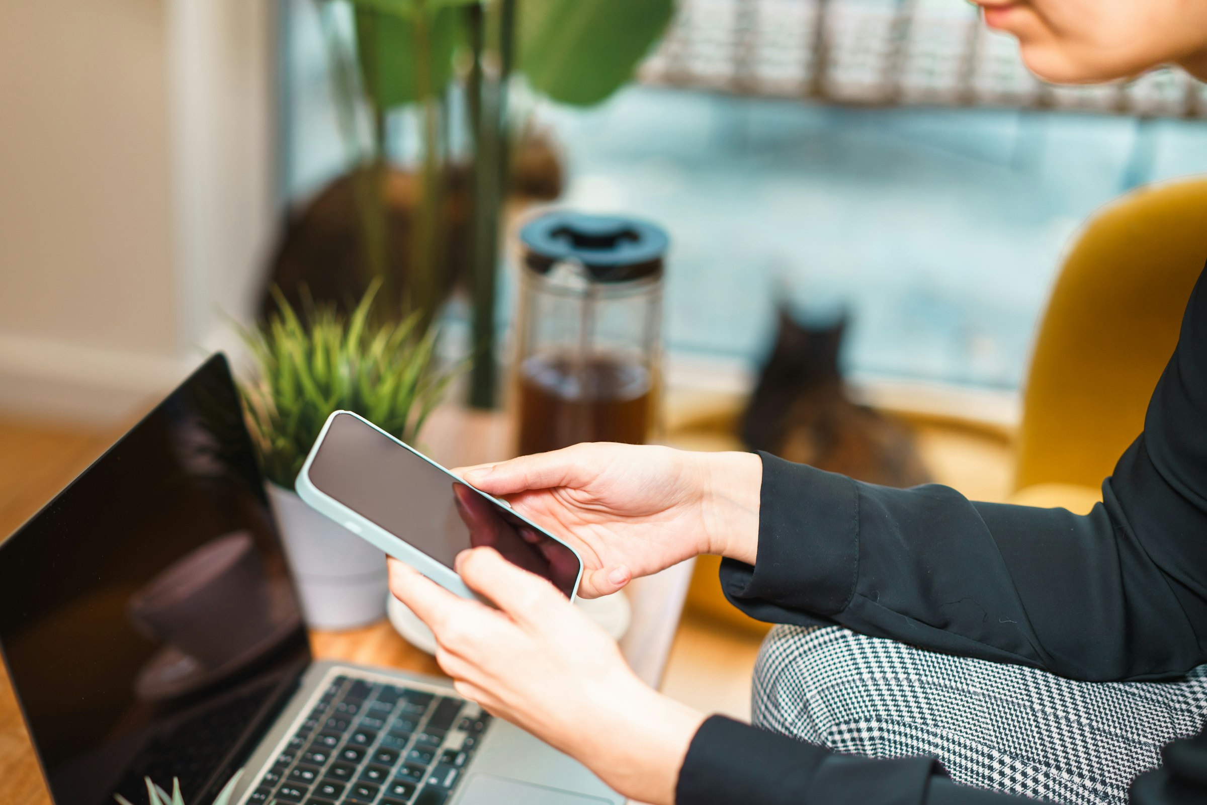 A person checking a smartphone while working at a laptop