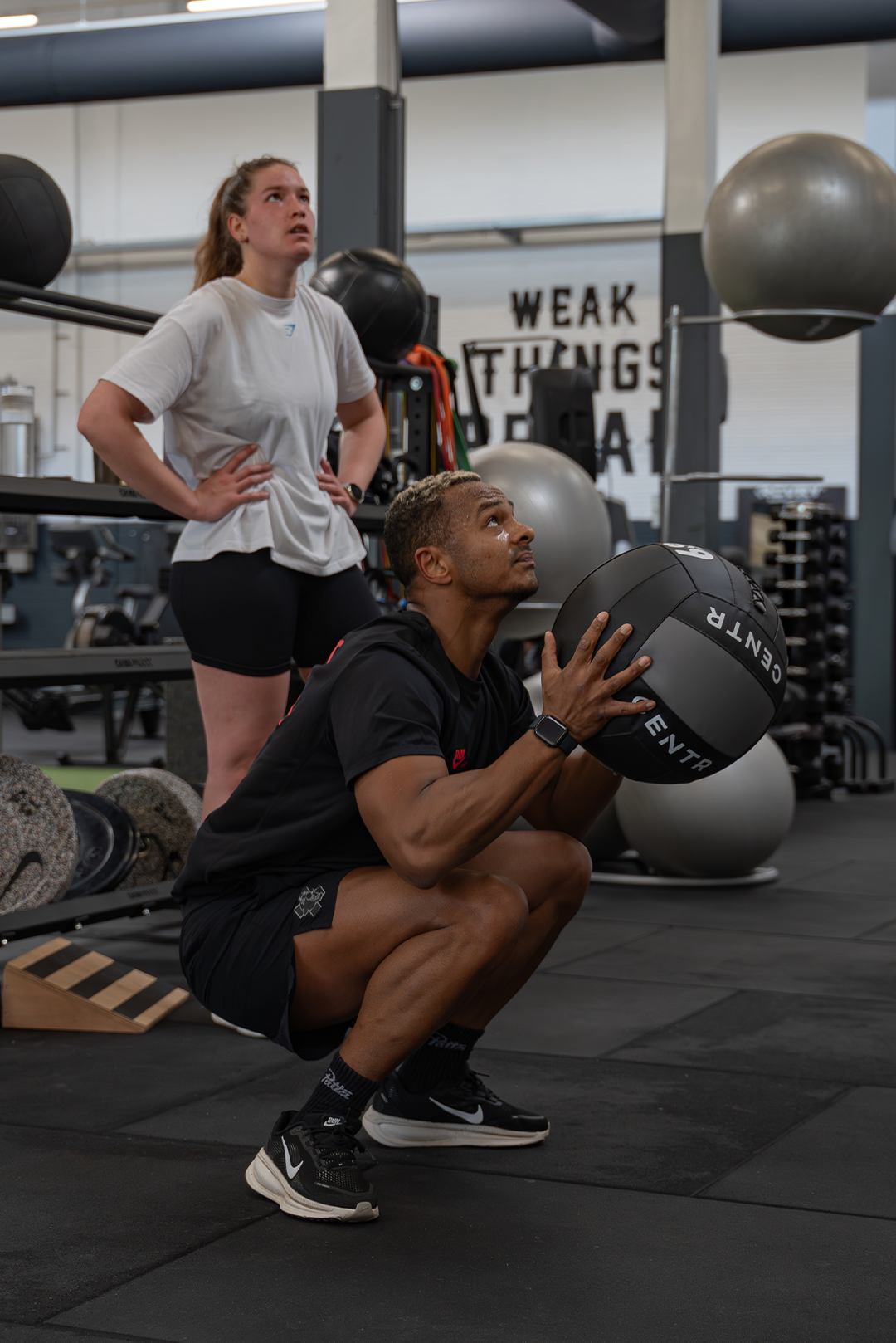 Smiling man in an orange patterned sweater sitting indoors with arms crossed.