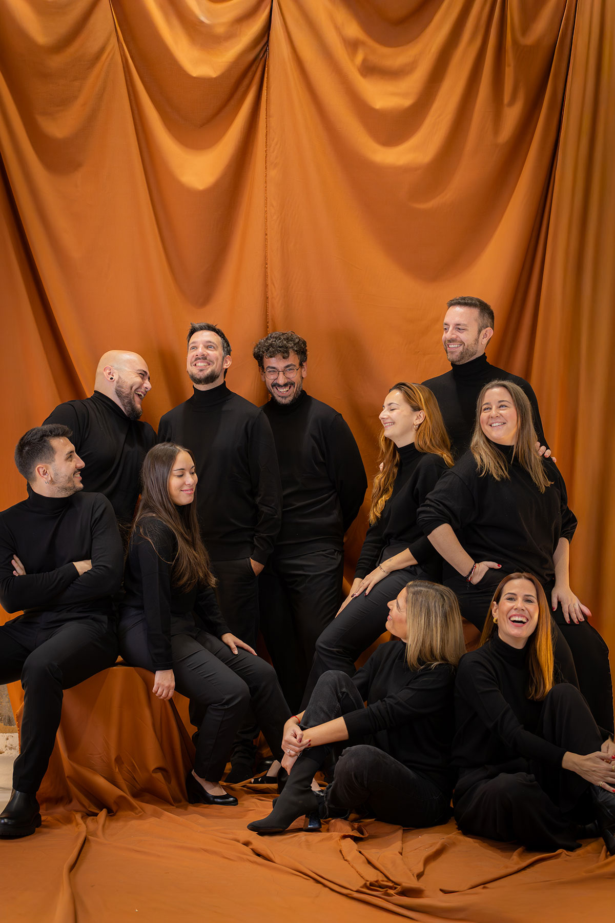 Grupo de diez personas sonrientes con ropa negra posando frente a una tela naranja.