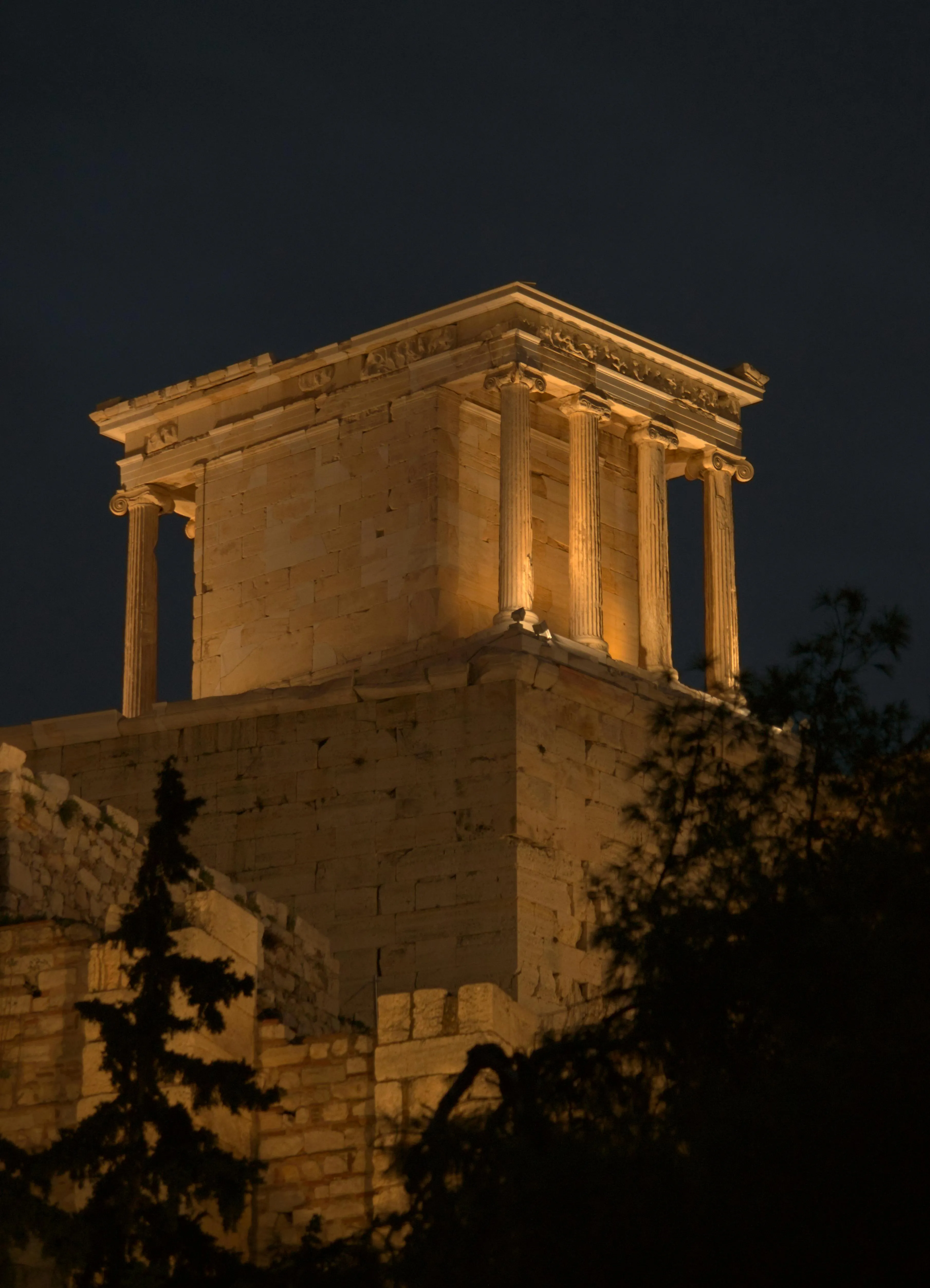 Illuminated ancient Greek temple with tall columns at night against a dark sky.