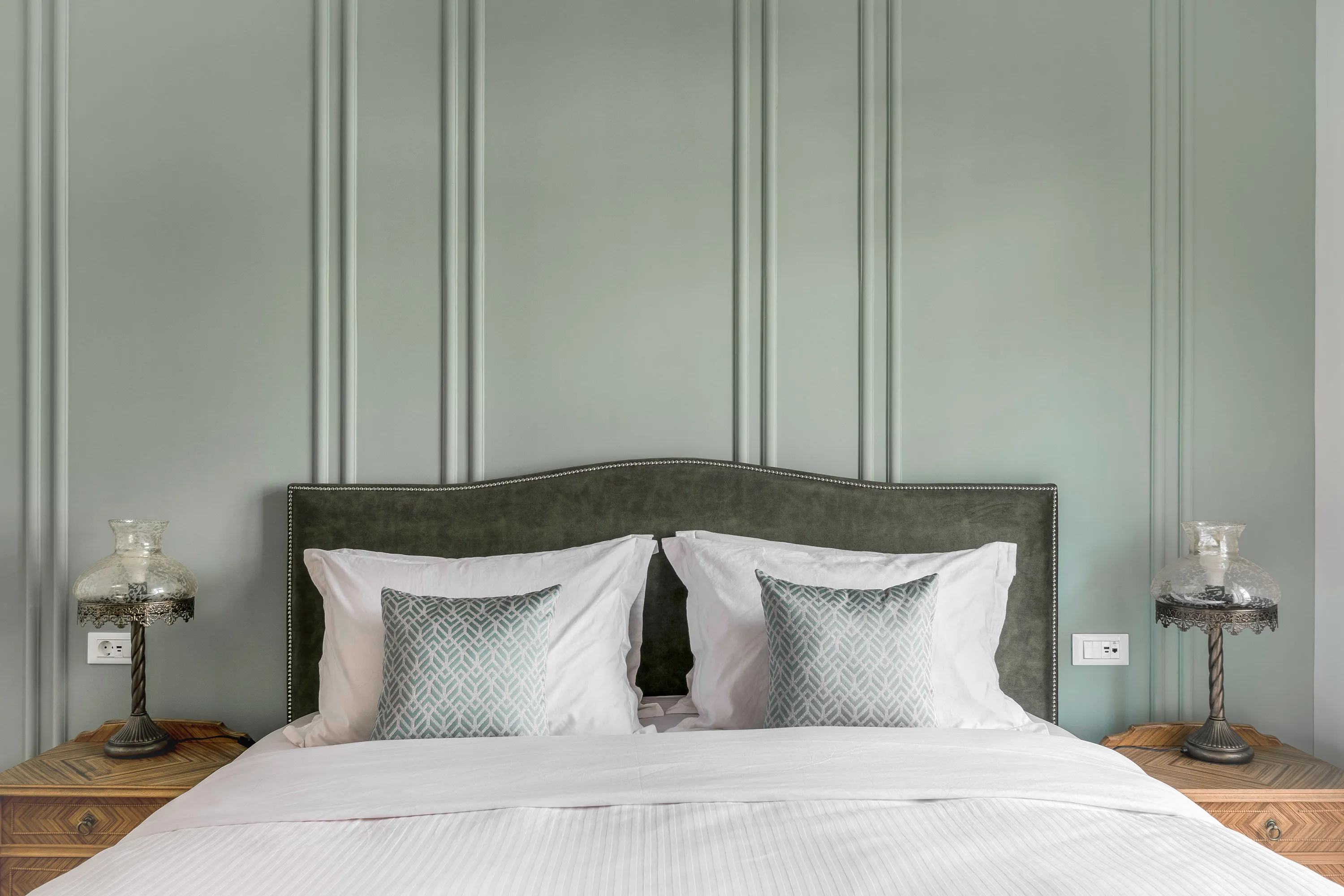 Elegant master bedroom at The Halo Collection boutique apartment in Athens, with paneled sage wall, upholstered headboard and crisp white bedding.