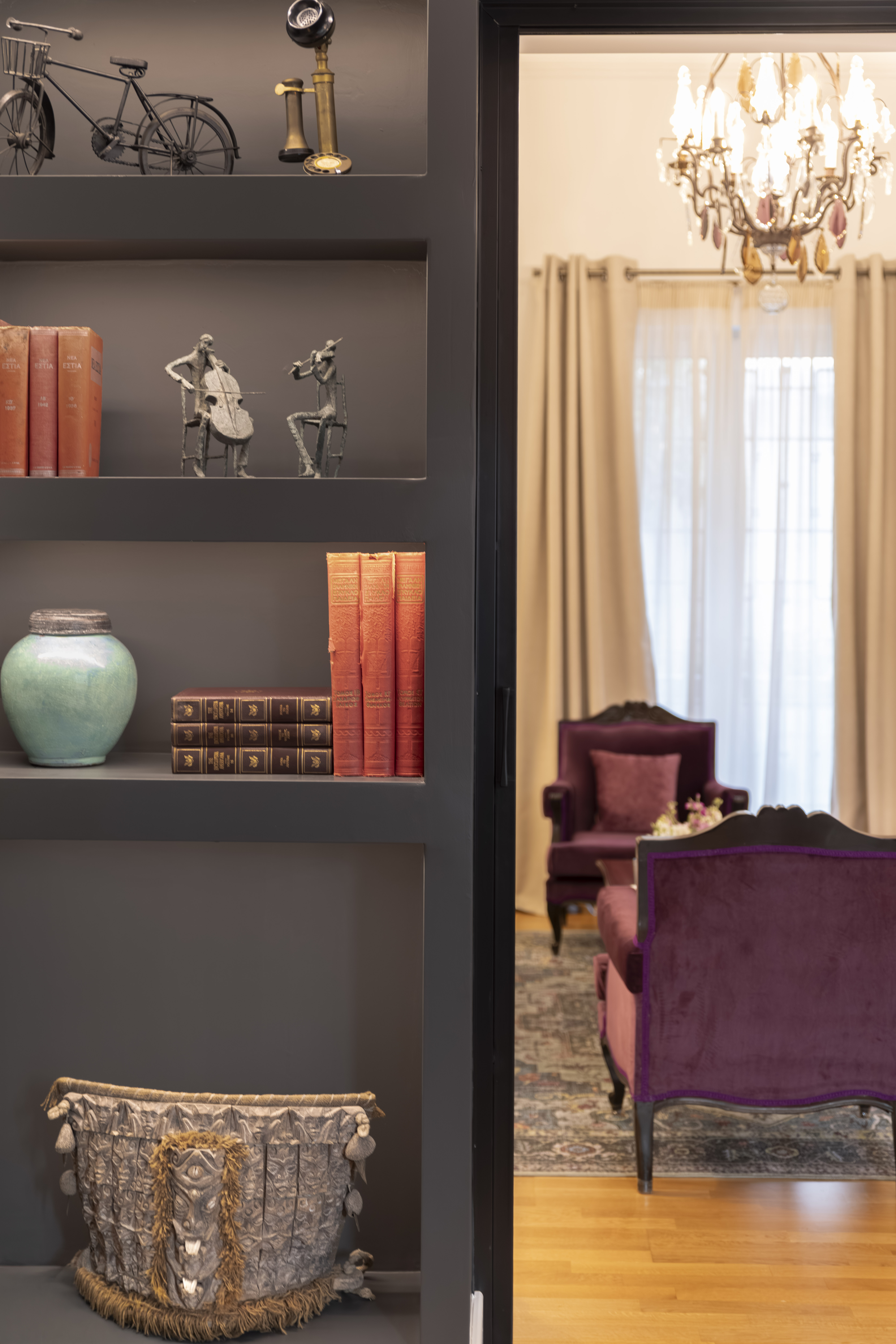 Mustard yellow armchair with a red floral cushion next to a glass-top table holding a vase of white and purple flowers and stacked books.