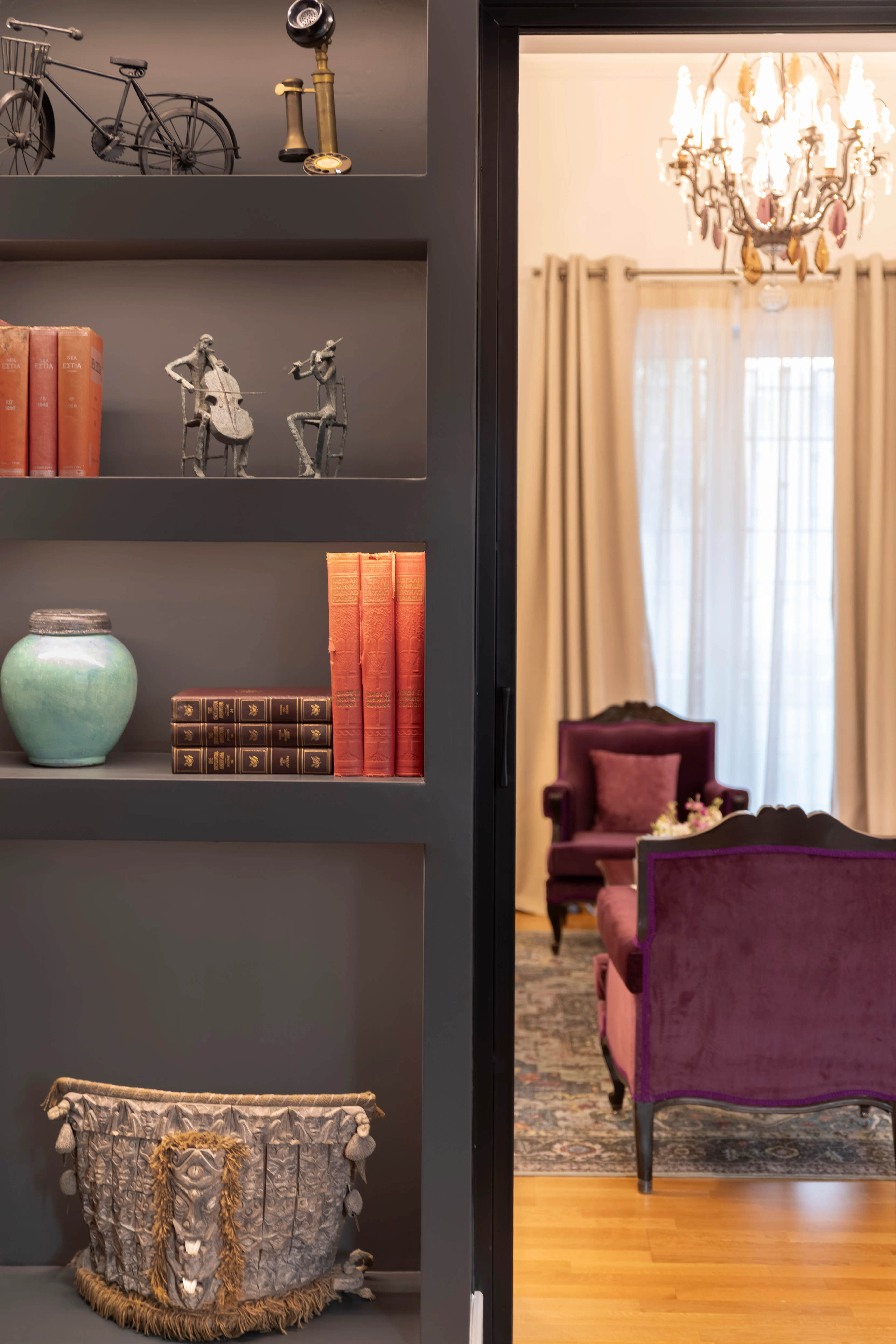 Mustard yellow armchair with a red floral cushion next to a glass-top table holding a vase of white and purple flowers and stacked books.