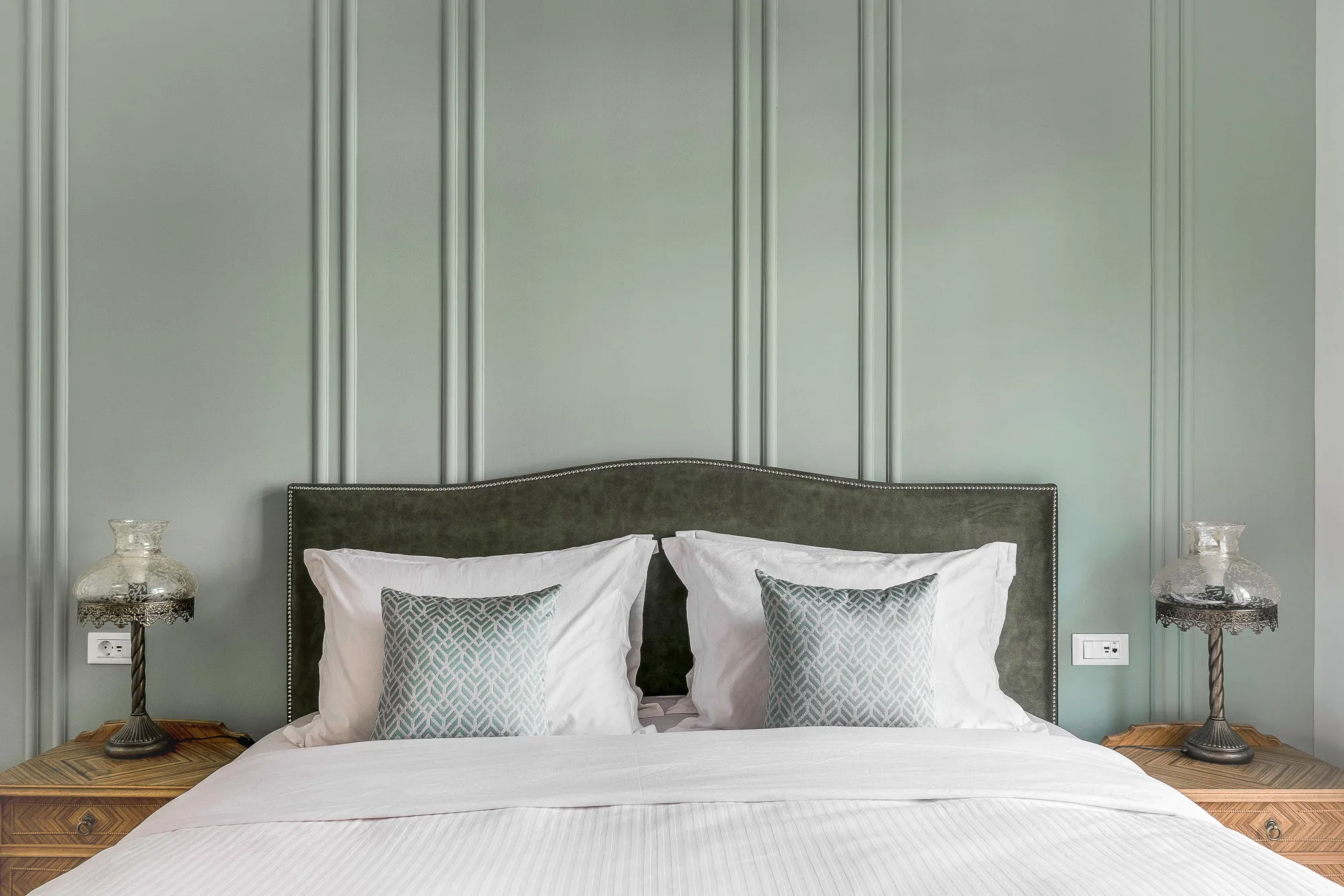 Elegant master bedroom at The Halo Collection boutique apartment in Athens, with paneled sage wall, upholstered headboard and crisp white bedding.