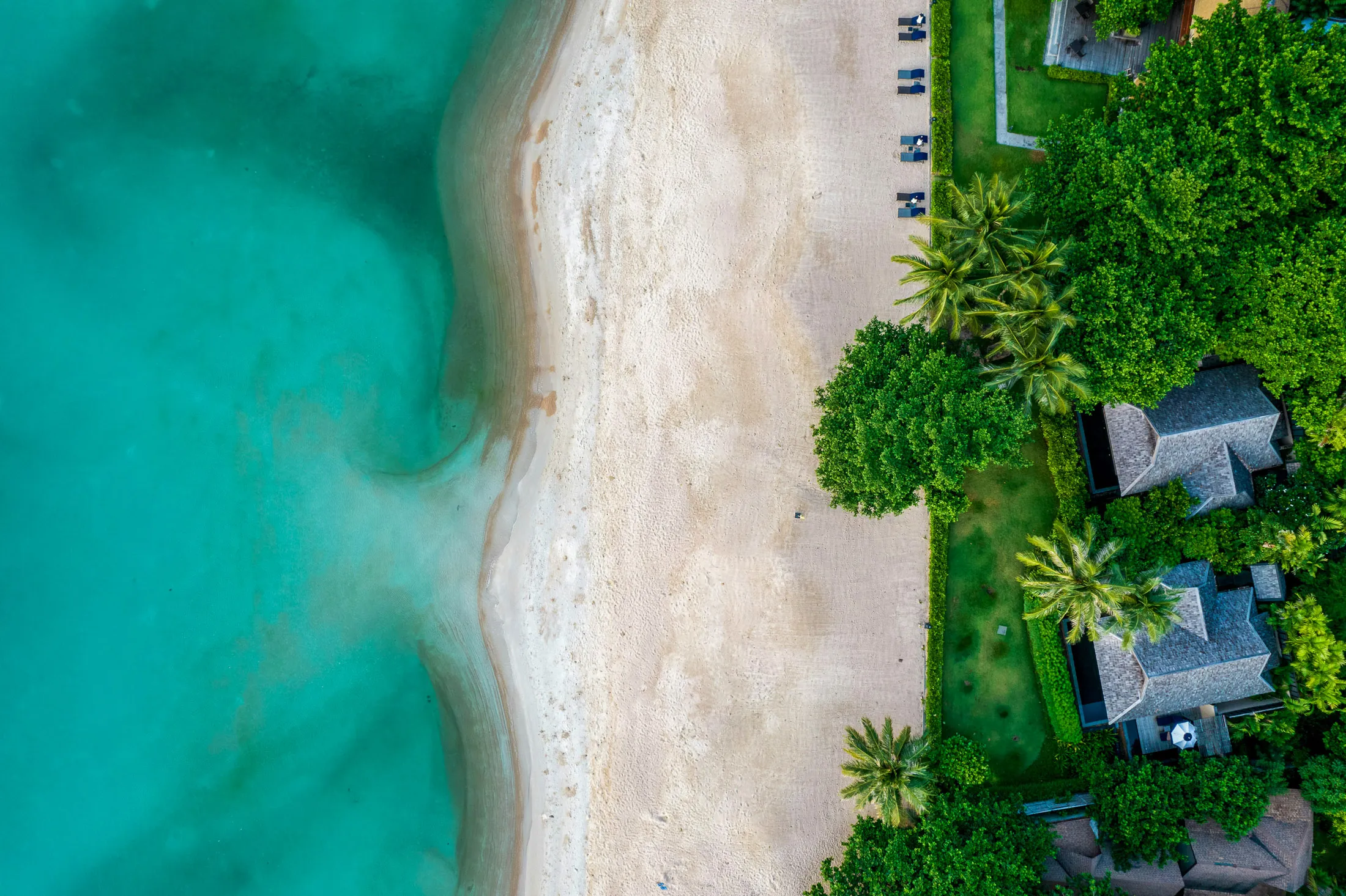 Aerial view of a beachfront villa with turquoise water and tropical greenery, representing luxury partner stays.