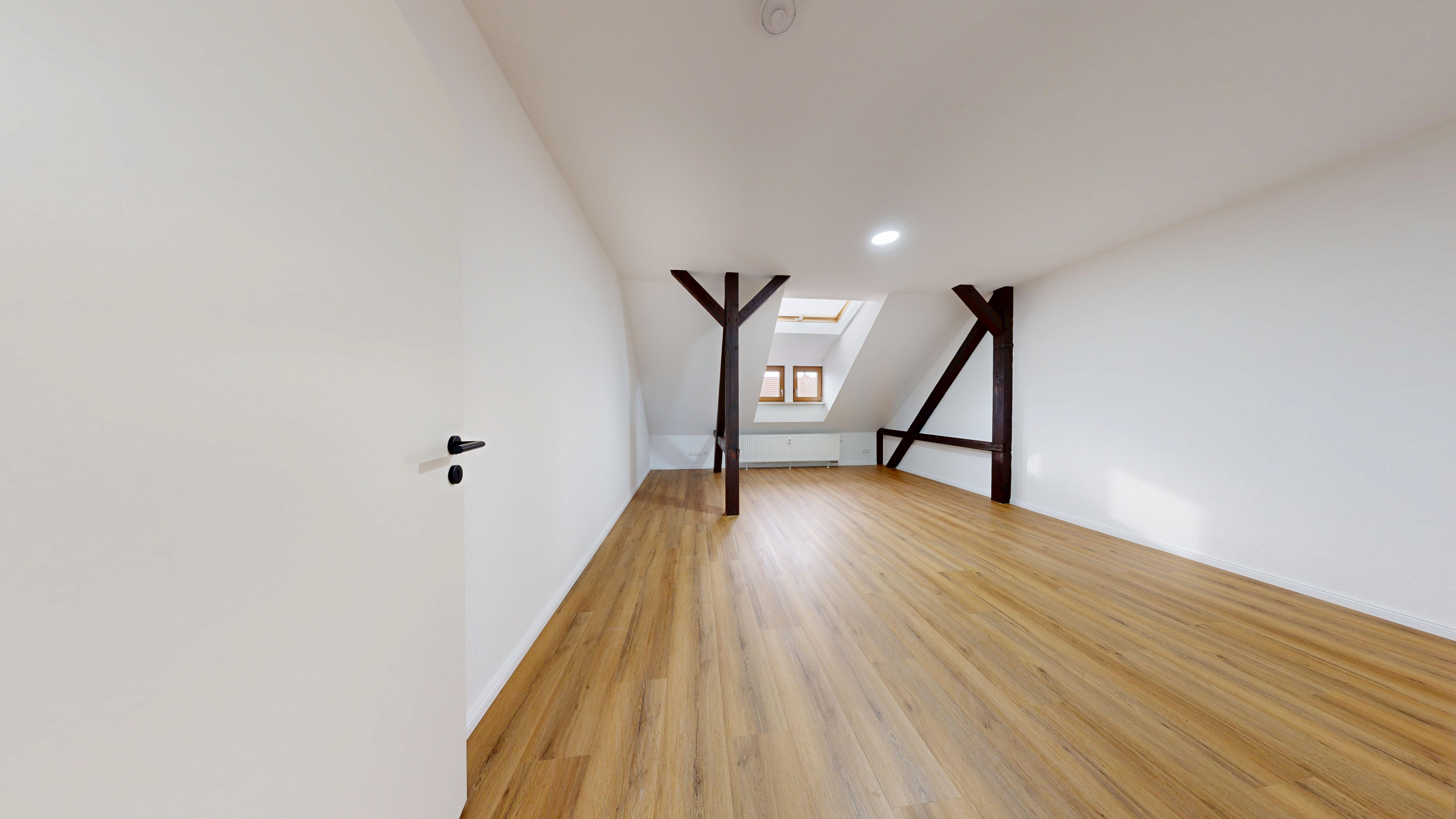 Dachgeschosszimmer nach der Sanierung mit Designboden in Eichenoptik und sichtbarem Gebälk