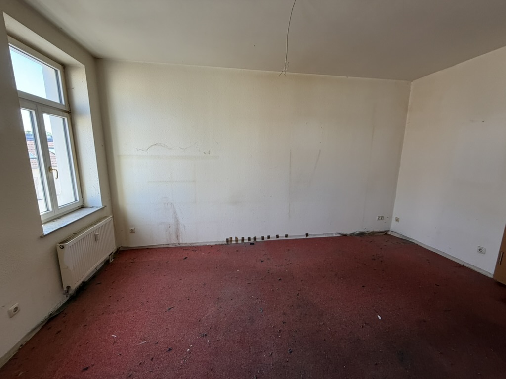Zimmer vor der Sanierung mit rotem Teppichboden und abgerissenen Sockelleisten