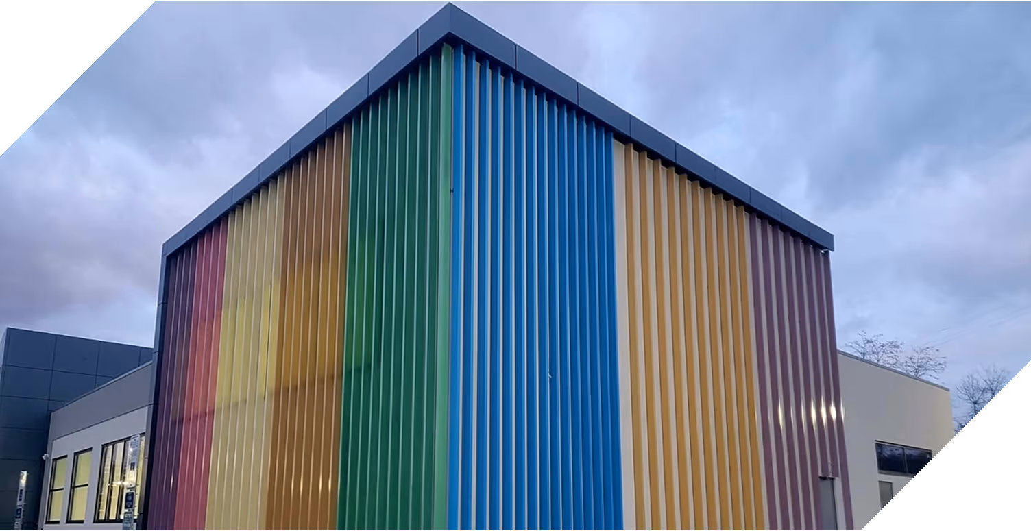 Modern building corner with vertical metal panels painted in rainbow colors under a cloudy sky.