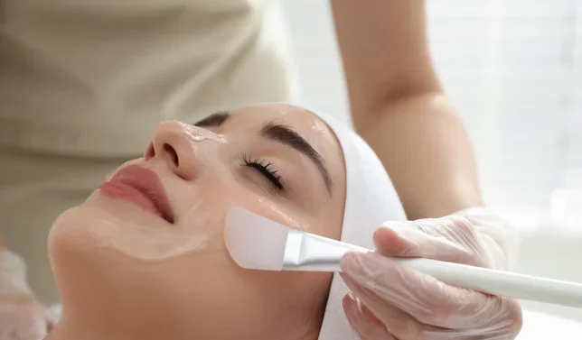 Une femme recevant un soin du visage avec une spatule appliquant un masque facial pendant un traitement de beauté.