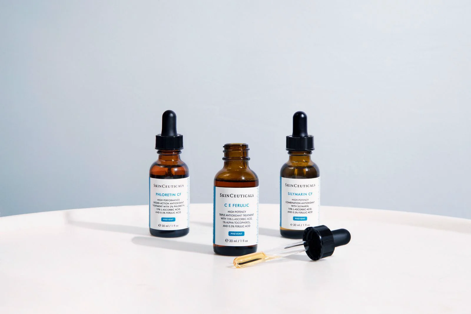 Trois flacons en verre ambré avec étiquettes SkinCeuticals contenant des sérums antioxydants avec compte-gouttes, posés sur une surface blanche. Clinique SkinIn, brossard