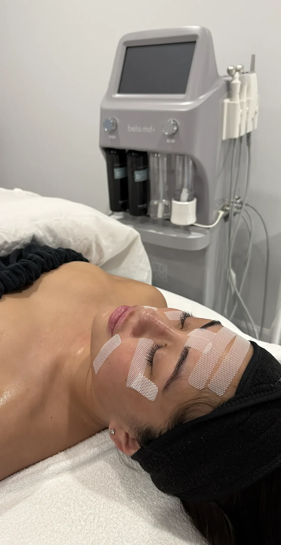 Femme allongée en traitement facial avec des patchs blancs sur le visage dans une clinique esthétique.