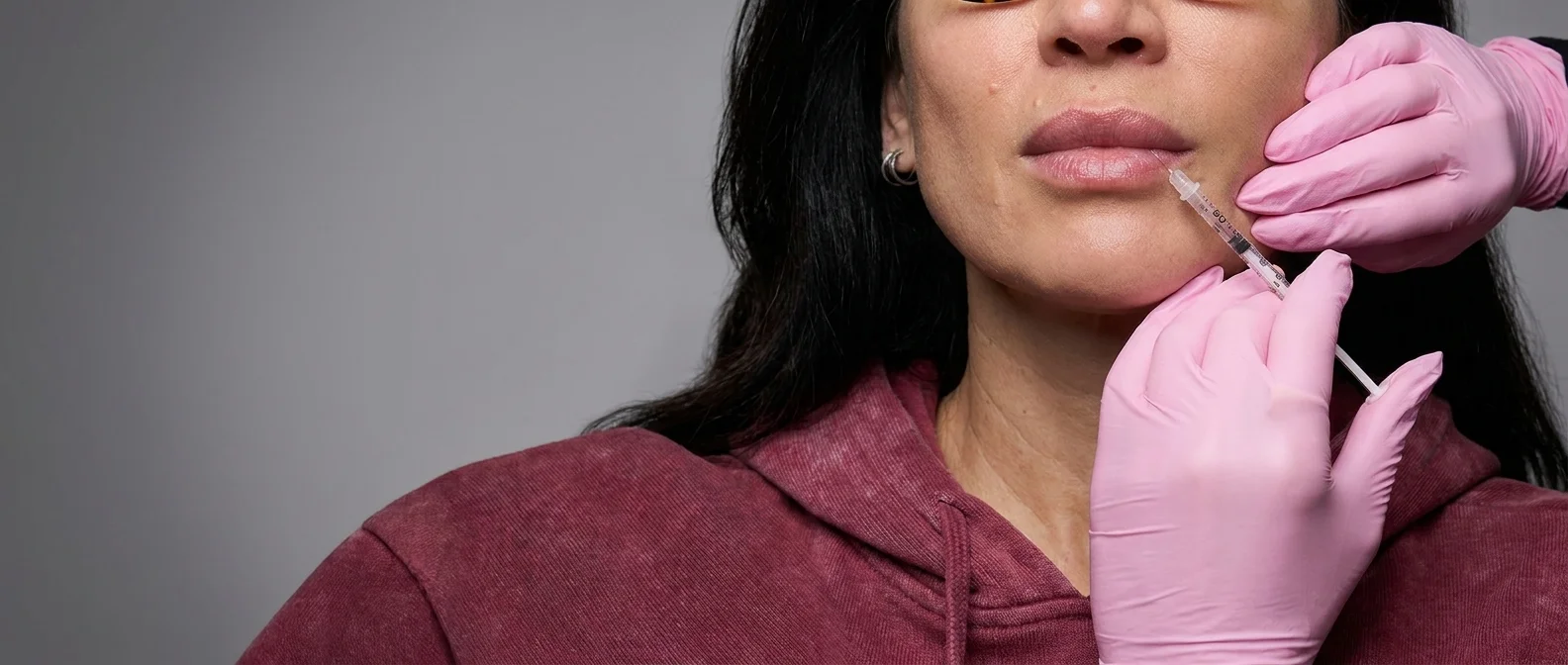 Une femme recevant une injection cosmétique sur les lèvres par une personne portant des gants roses.