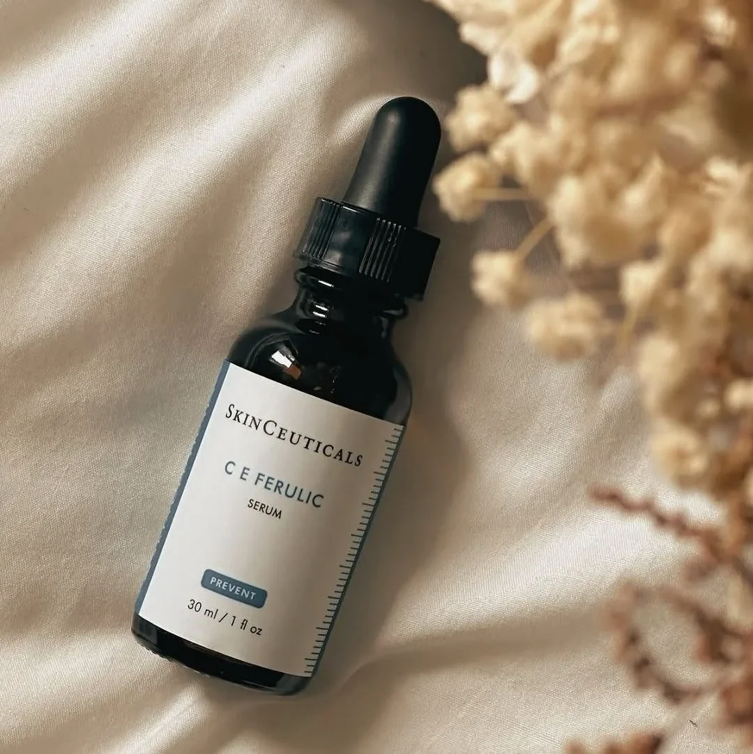 Flacon de sérum SkinCeuticals C E Ferulic de 30 ml avec compte-gouttes sur tissu beige à côté de fleurs séchées.