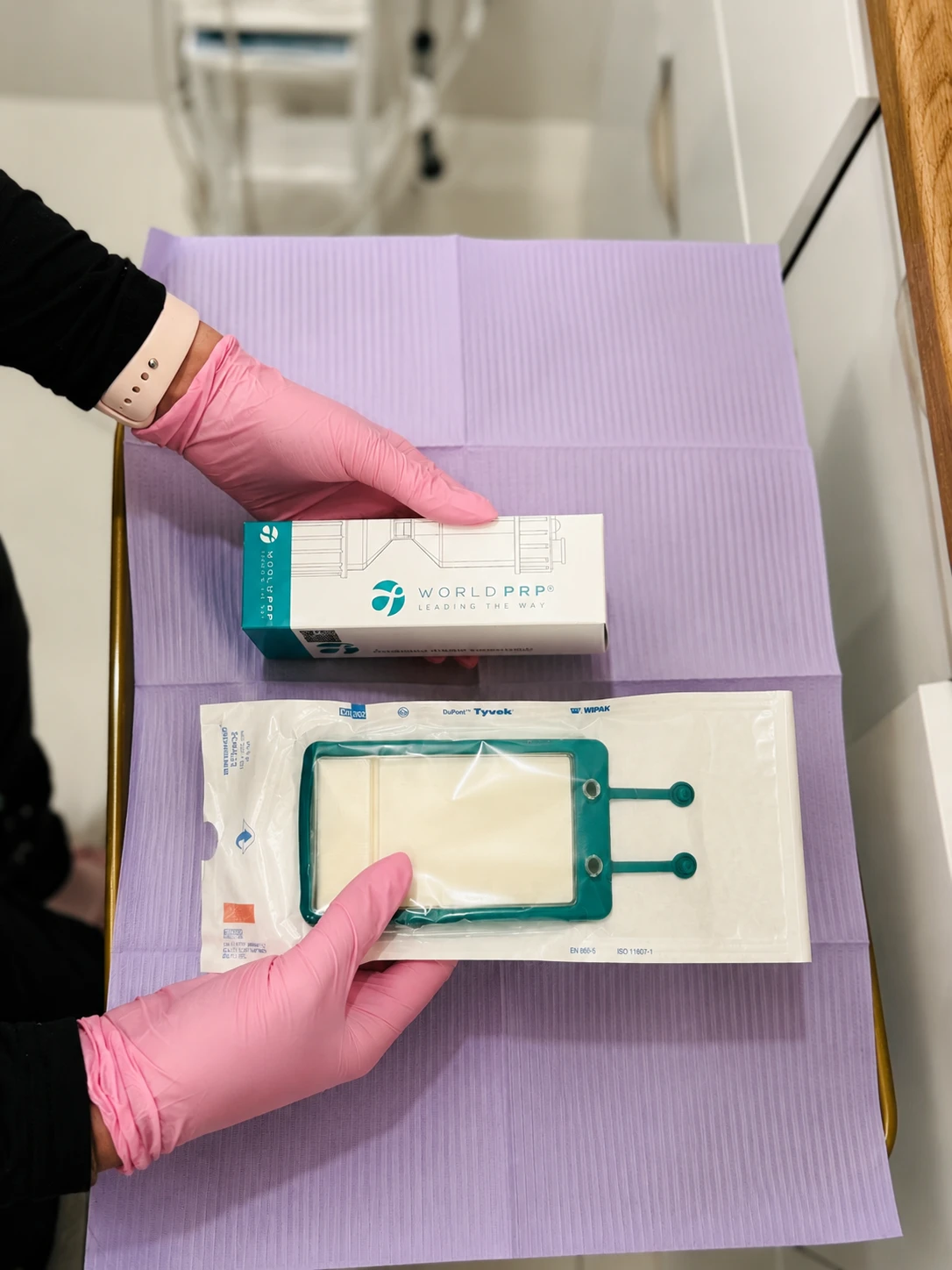 Une personne avec des gants roses tient un emballage et une boîte World PRP dans une clinique.