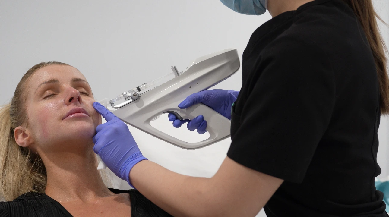 Une femme reçoit un traitement facial par un professionnel portant un masque et des gants bleus.