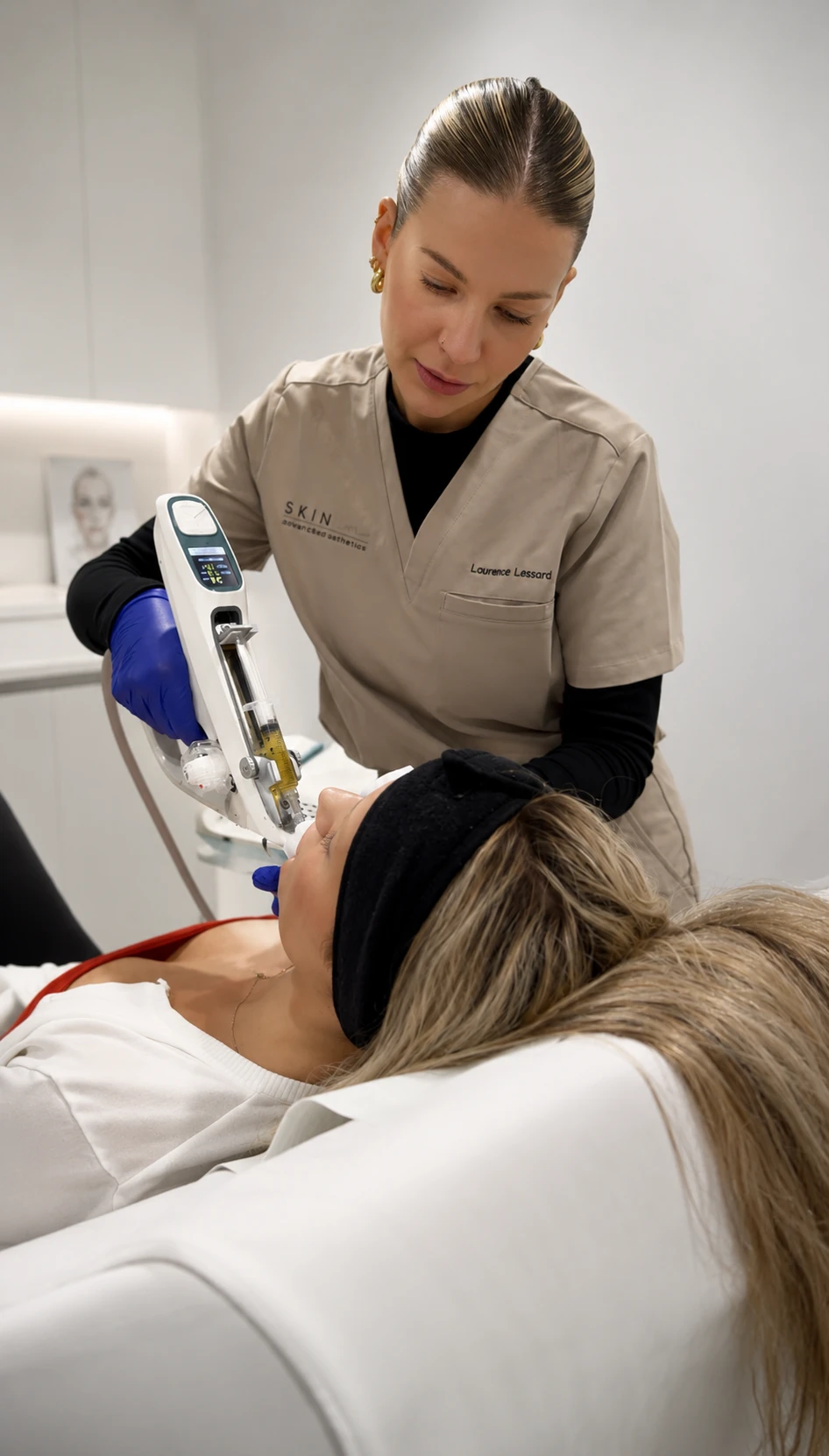 Esthéticienne effectuant un soin du visage avec un appareil à seringue sur une patiente allongée.