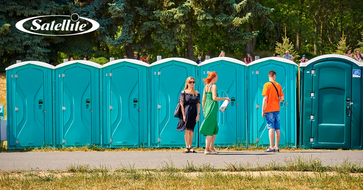 People standing outside a row of green Satellite Industries portable restrooms—including an ADA unit—at a busy outdoor event, illustrating demand and key client opportunities for local portable sanitation operators.