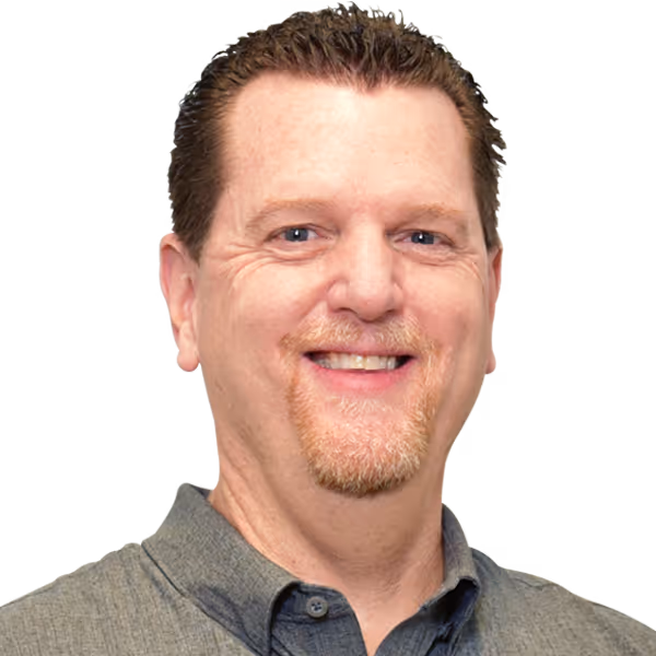 Smiling man with short brown hair and facial hair, wearing a gray collared shirt against a black