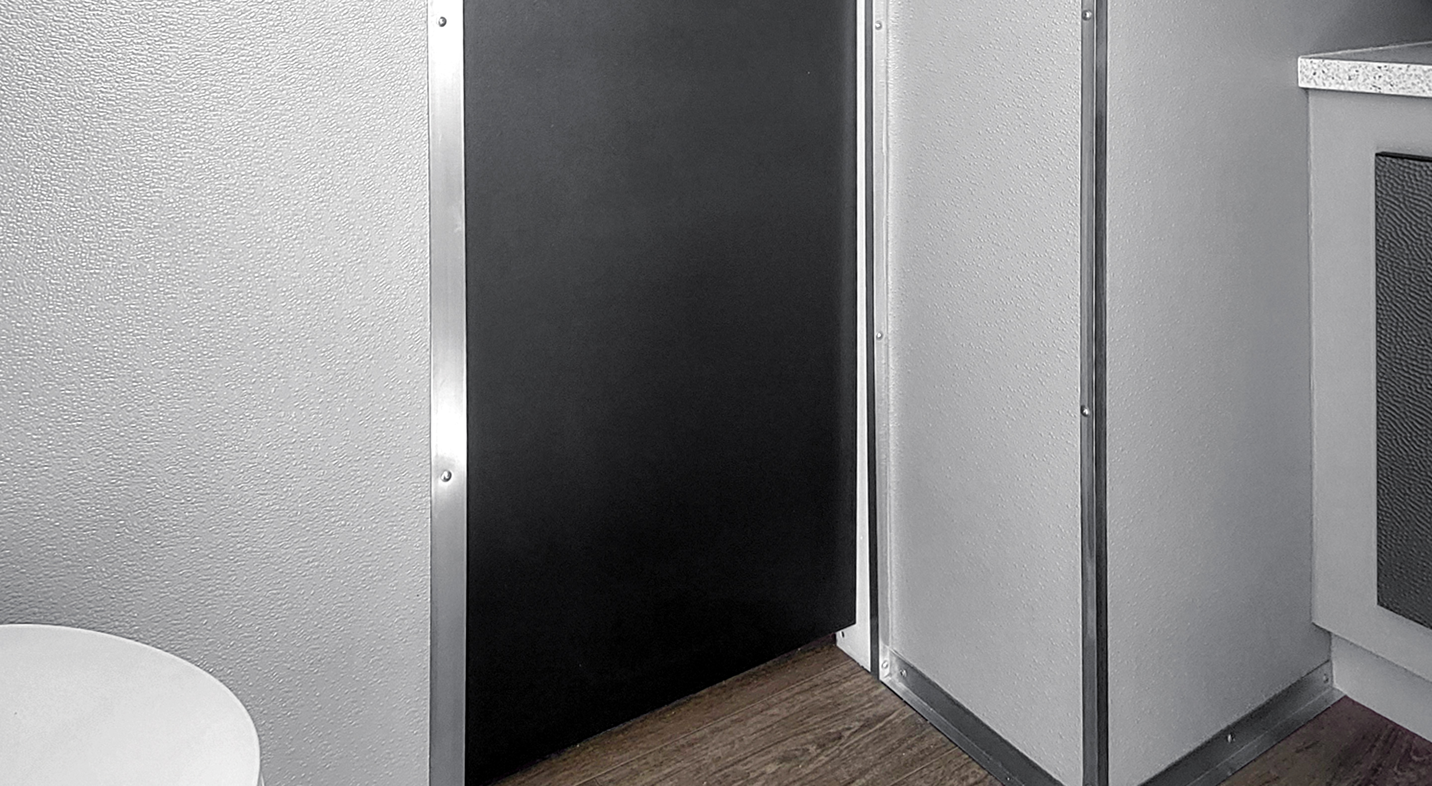 Black door next to a white toilet and a wall with wood floor below.