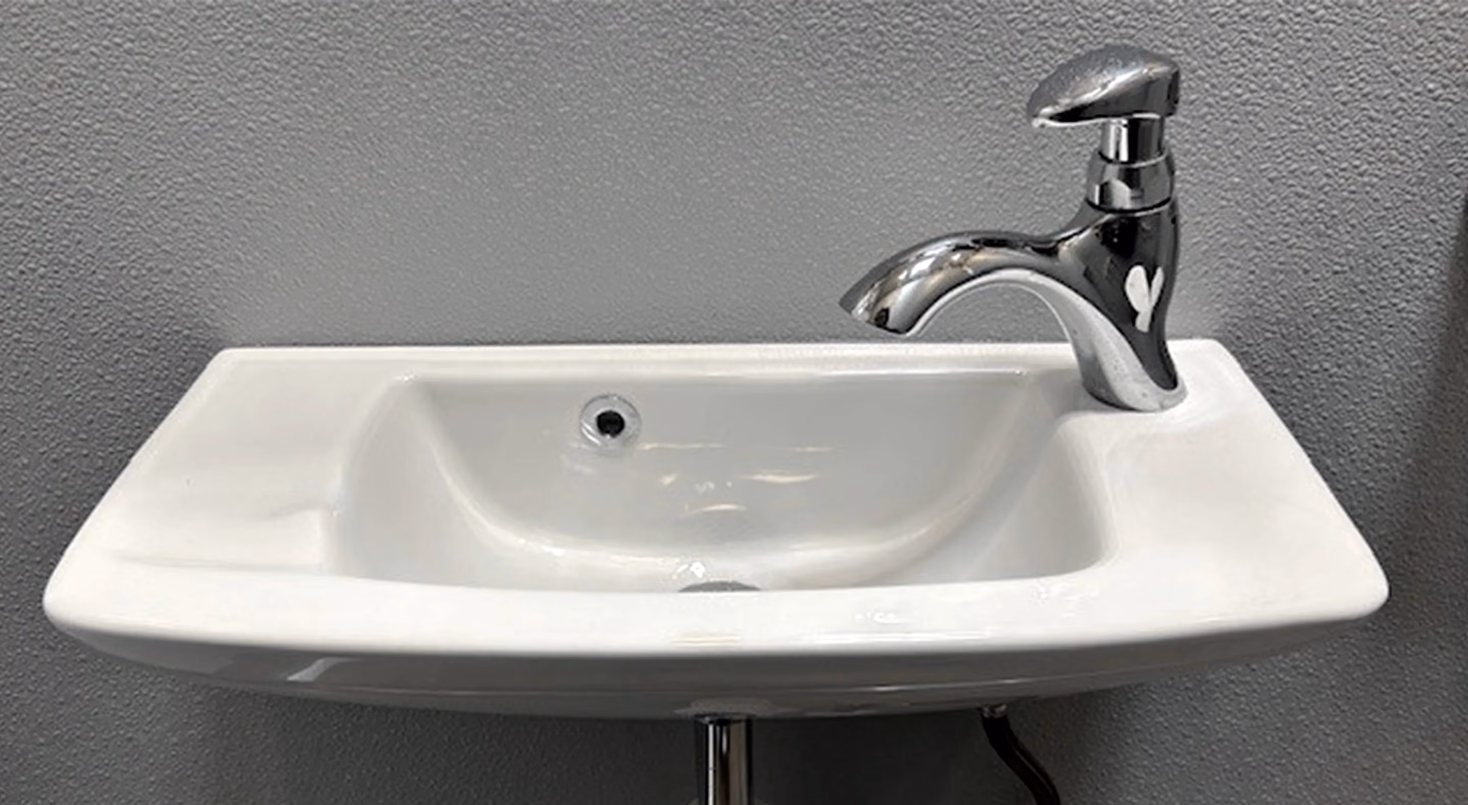Wall-mounted white ceramic sink with a curved silver faucet and a gray textured wall background.