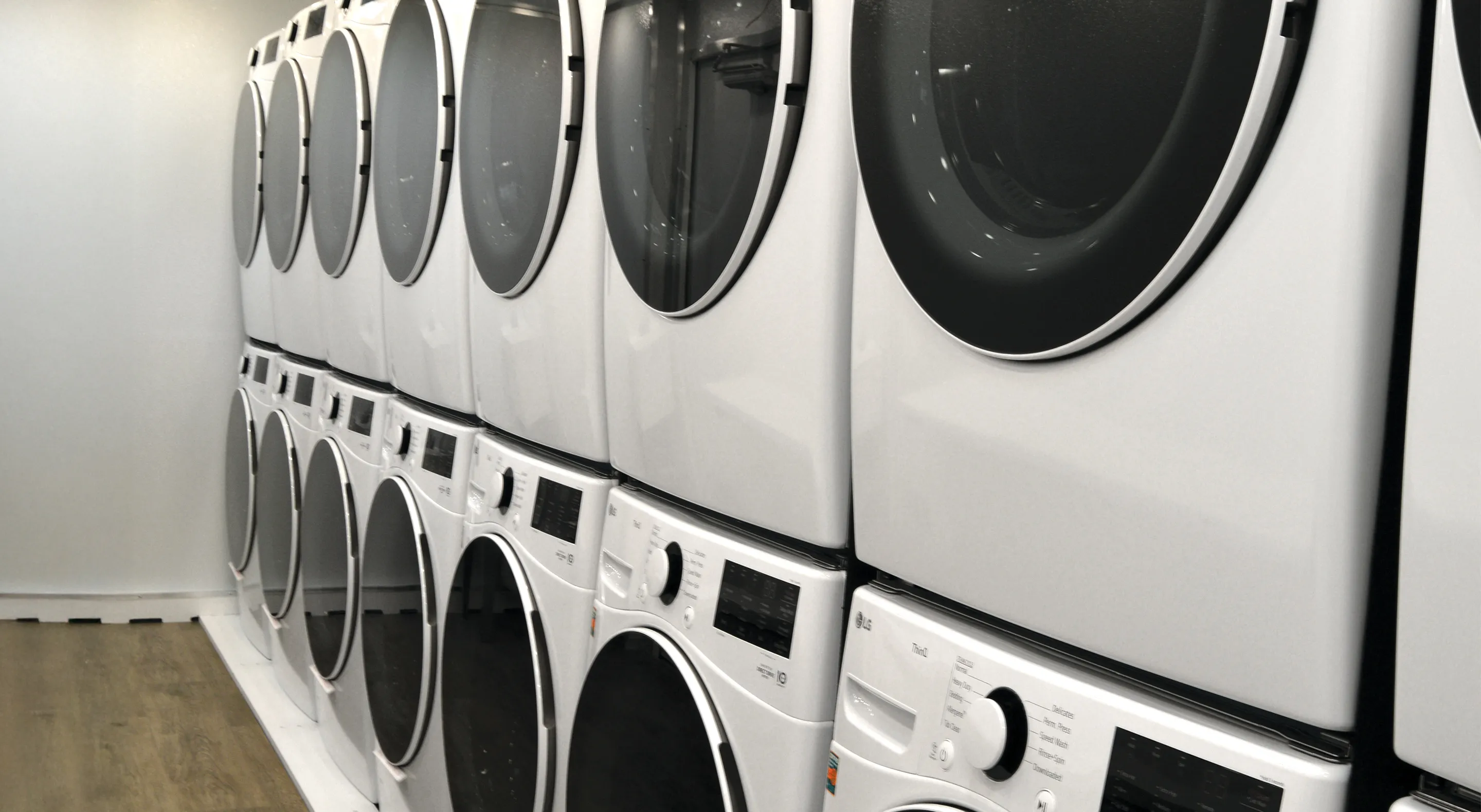 Two rows of stacked white front-loading washers and dryers in a modern laundry room.