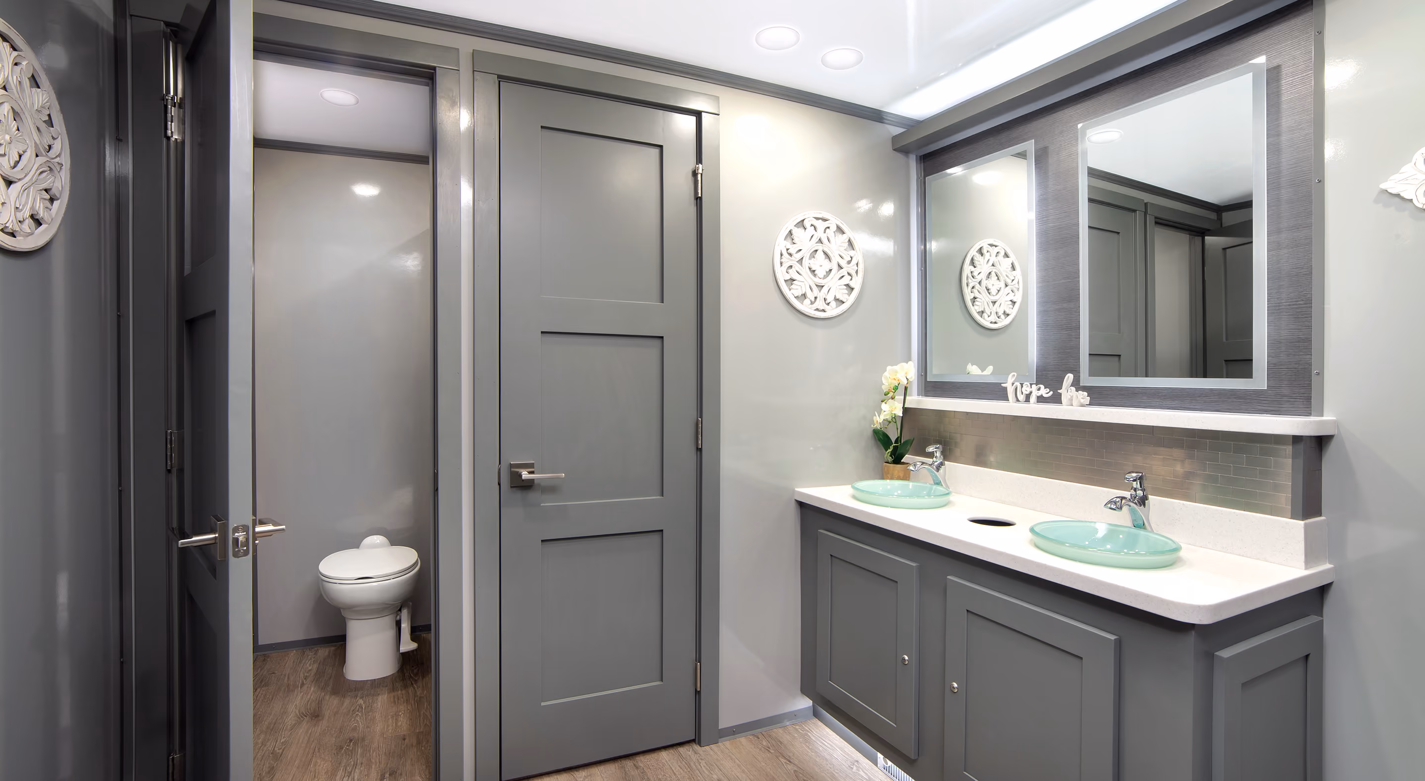 Modern bathroom with gray cabinetry, dual sinks, and a private toilet area. Decorated with wall art.