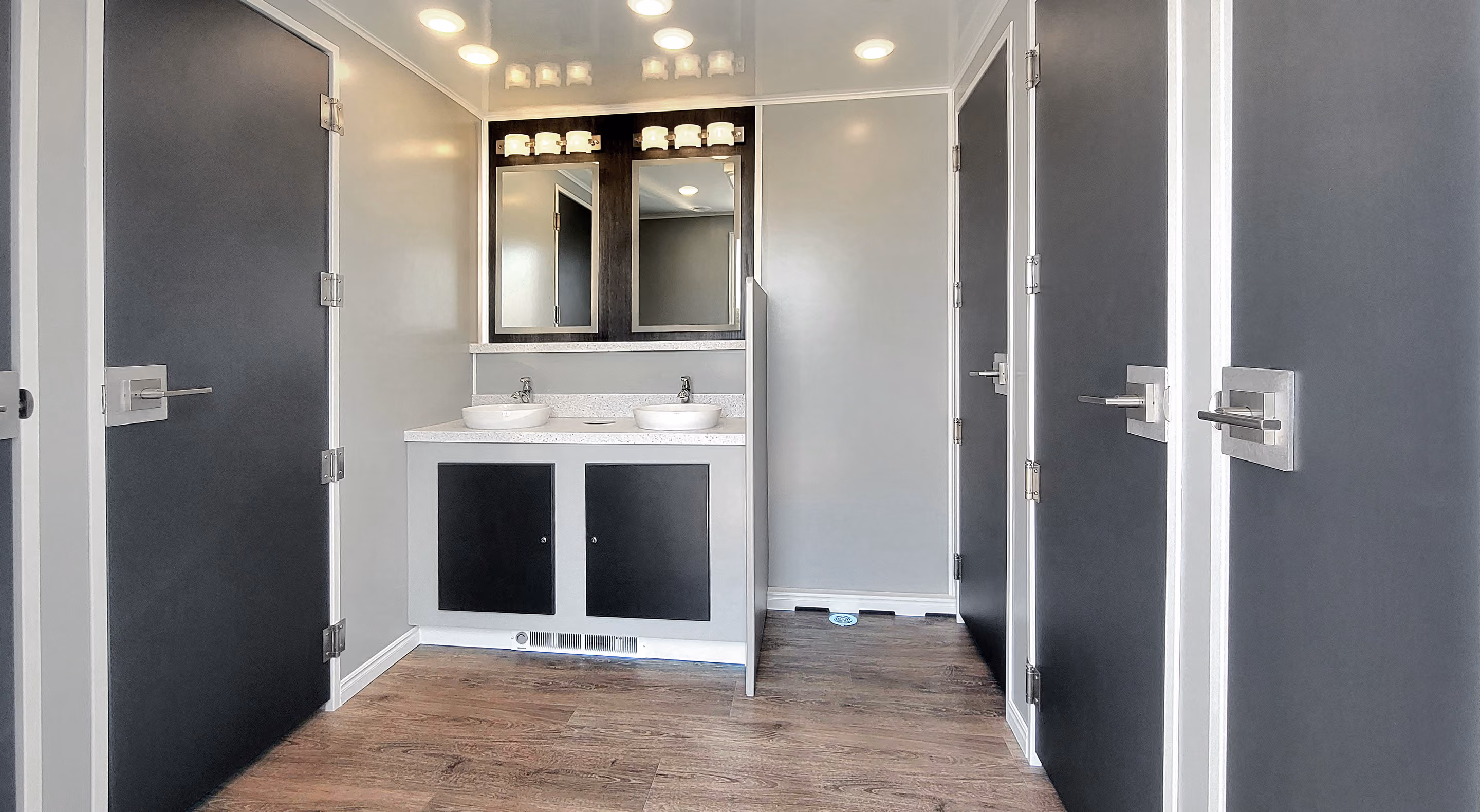Modern restroom featuring dual sinks, stylish mirrors, and dark cabinetry with light fixtures above.