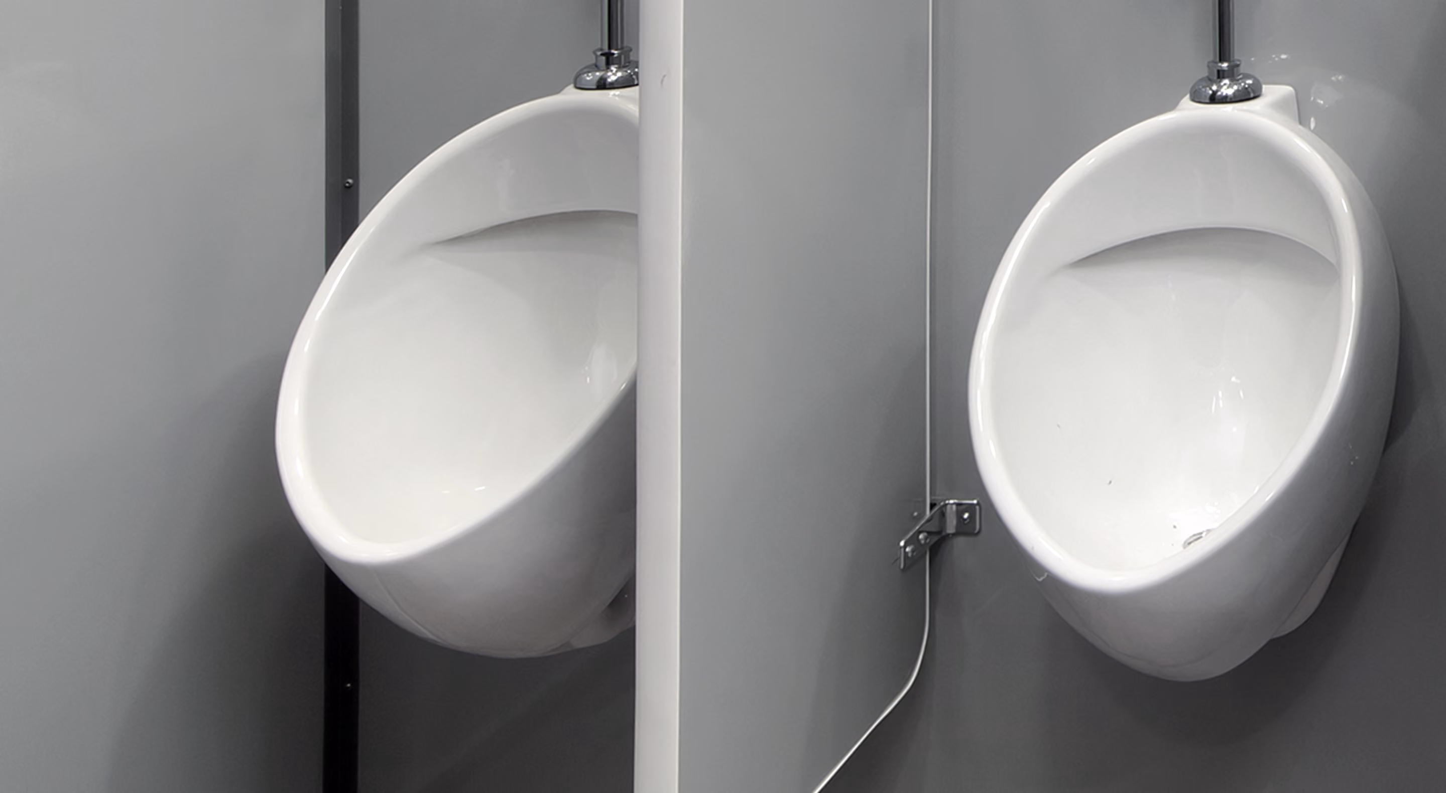 Two white ceramic urinals mounted on a gray wall with a privacy divider between them.