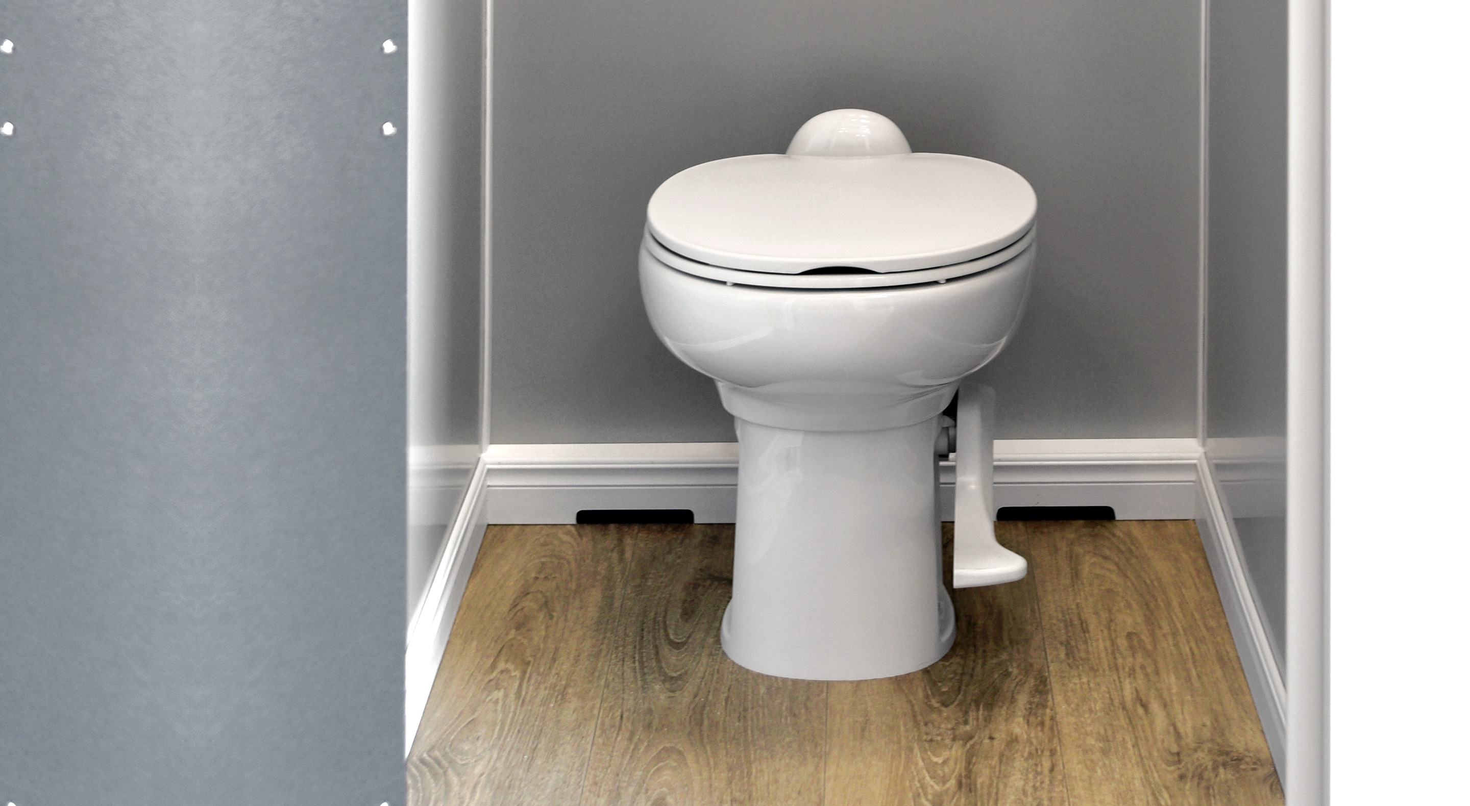 A white toilet in a minimalistic bathroom with wooden flooring and gray walls.