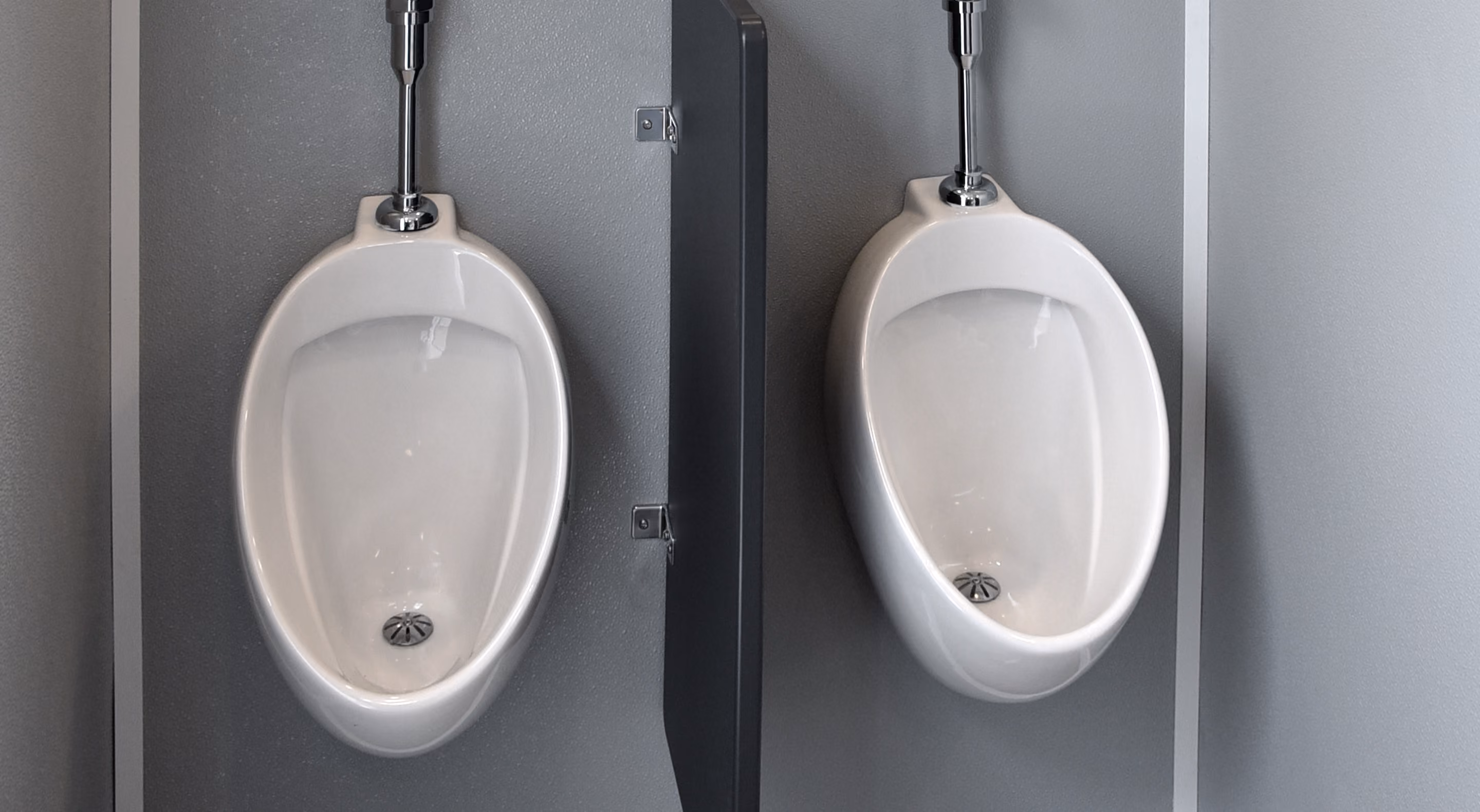 Two white urinals separated by a gray privacy divider in a modern restroom.
