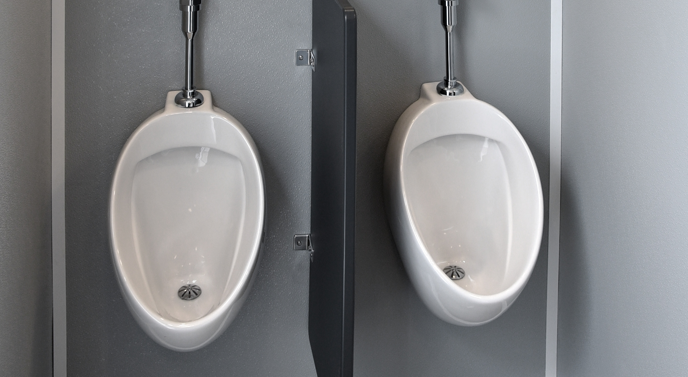 Two white urinals separated by a gray privacy divider in a modern restroom.
